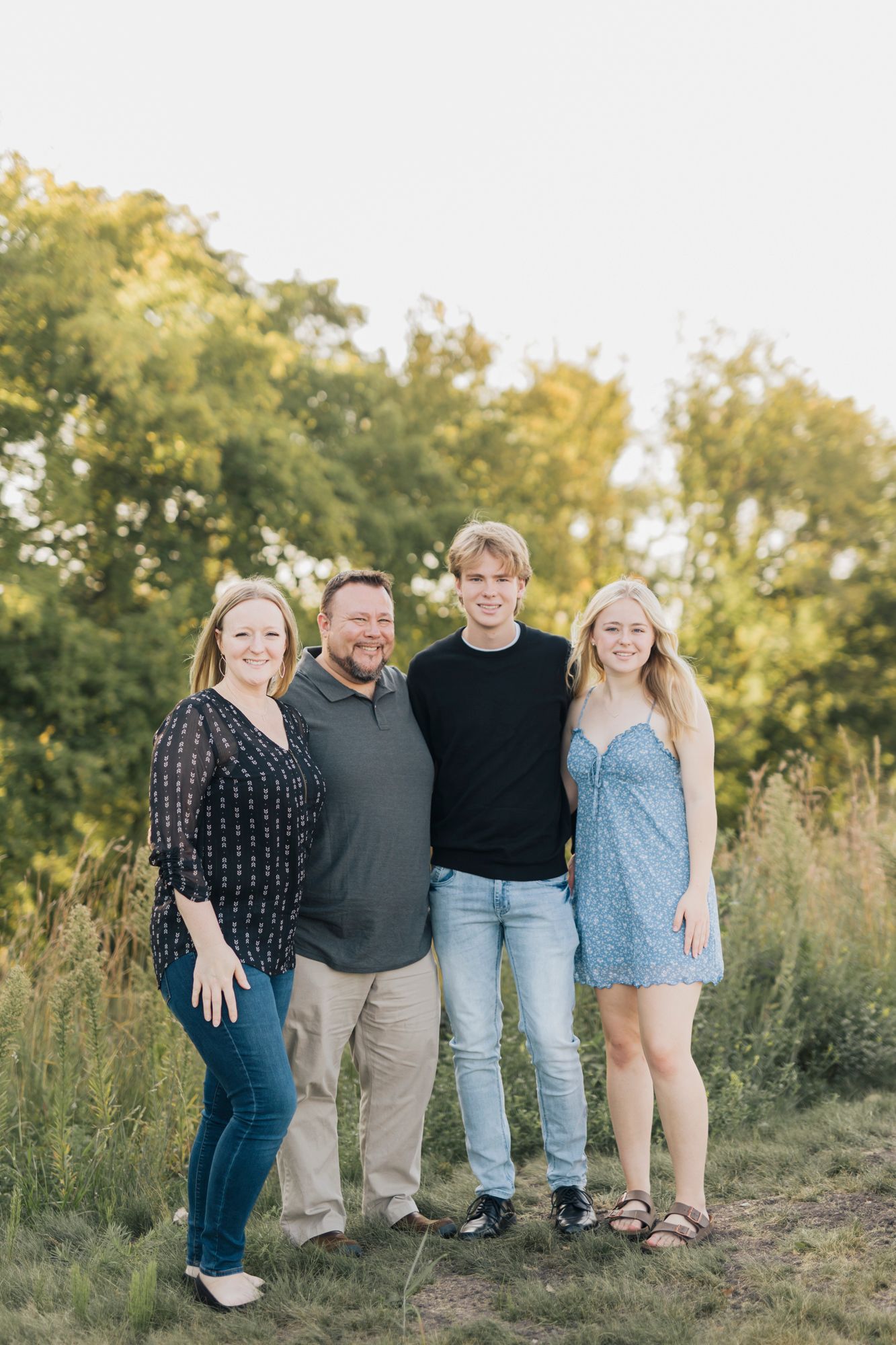 Family of four poses together outdoors during golden hour in casual attire.