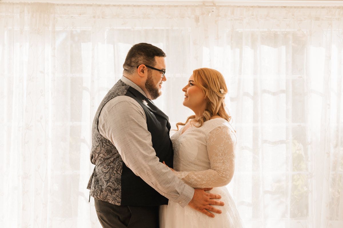 Couple dances together in bright indoor setting with white curtained windows.