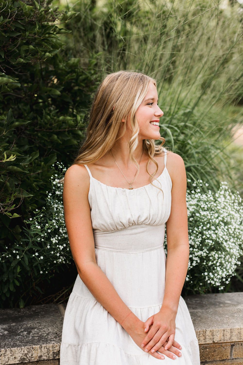 A white summer dress contrasts beautifully with lush garden greenery in an outdoor portrait.