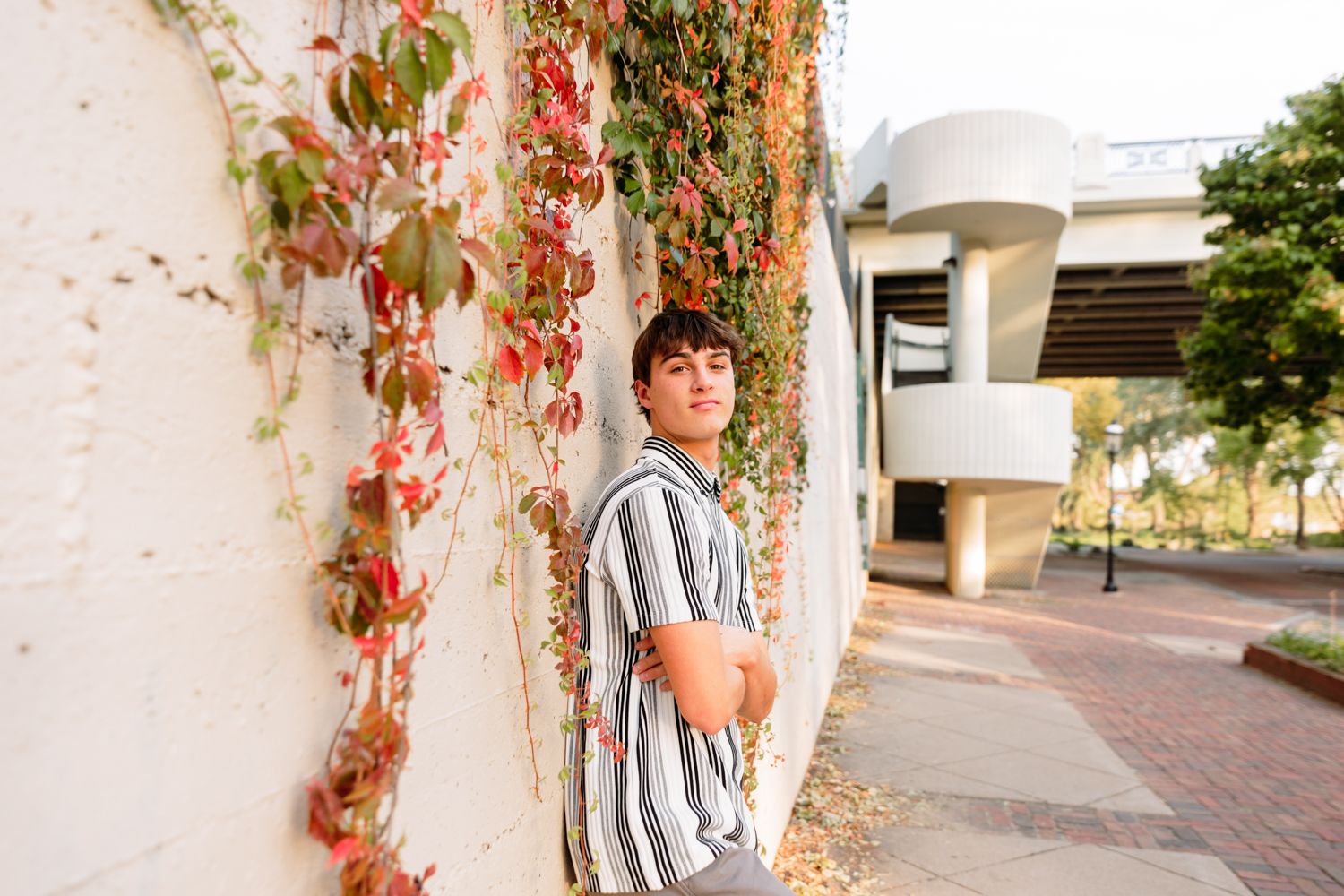 Striped shirt figure poses against a backdrop of climbing red vines on an exterior wall.
