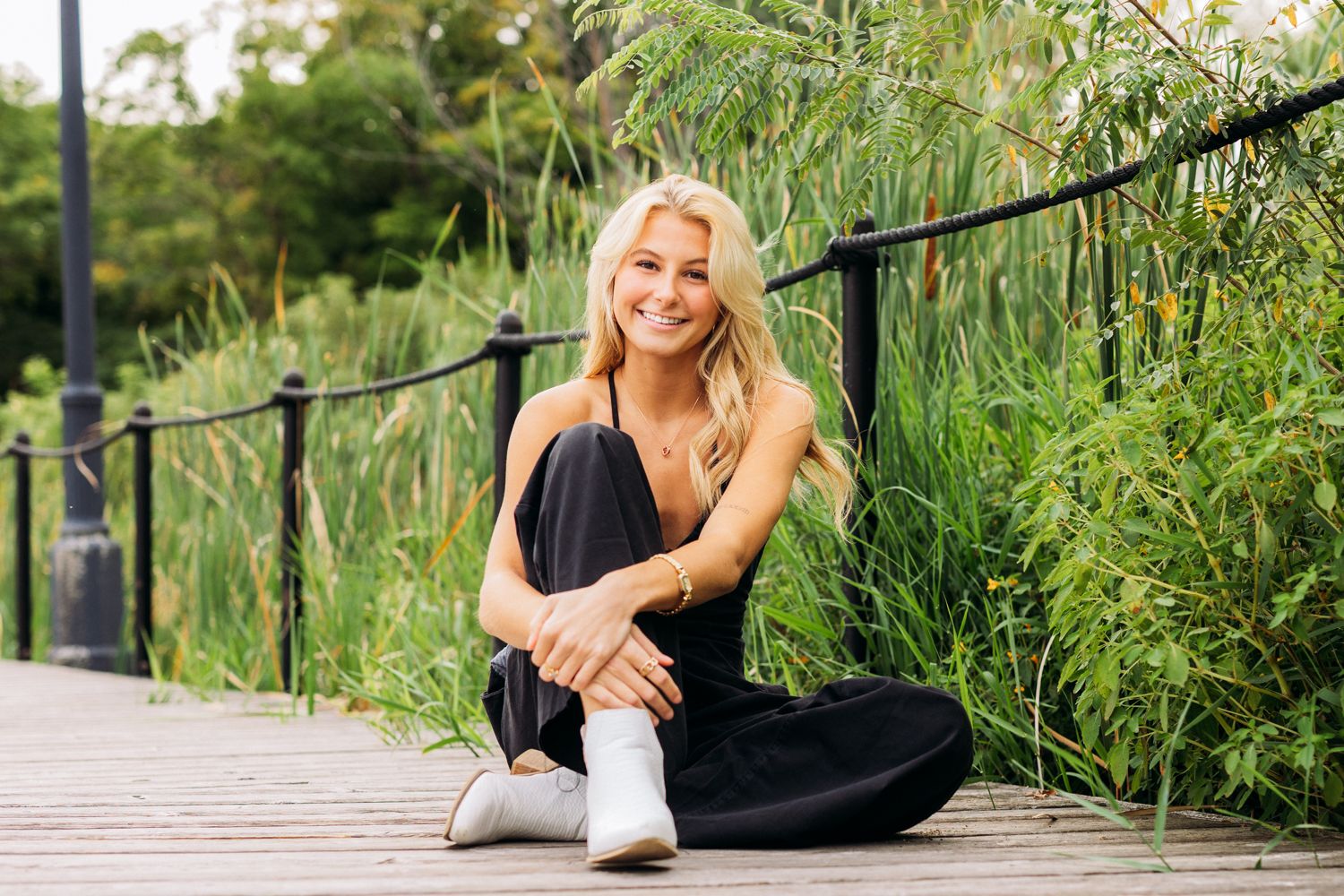 Color photos of someone in casual wear sitting on a wooden boardwalk surrounded by tall green grasses.