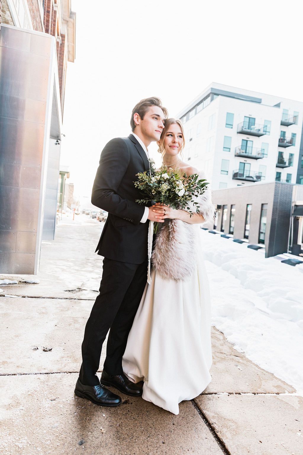 Couple shares intimate moment in urban setting during winter wedding photoshoot.