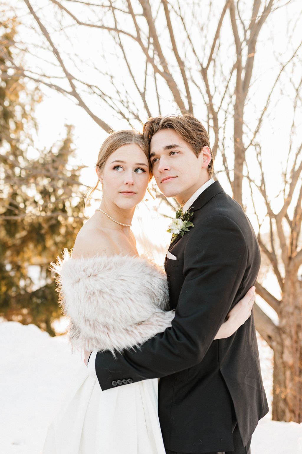 Newlyweds embrace for romantic portraits in a snow-covered winter setting.