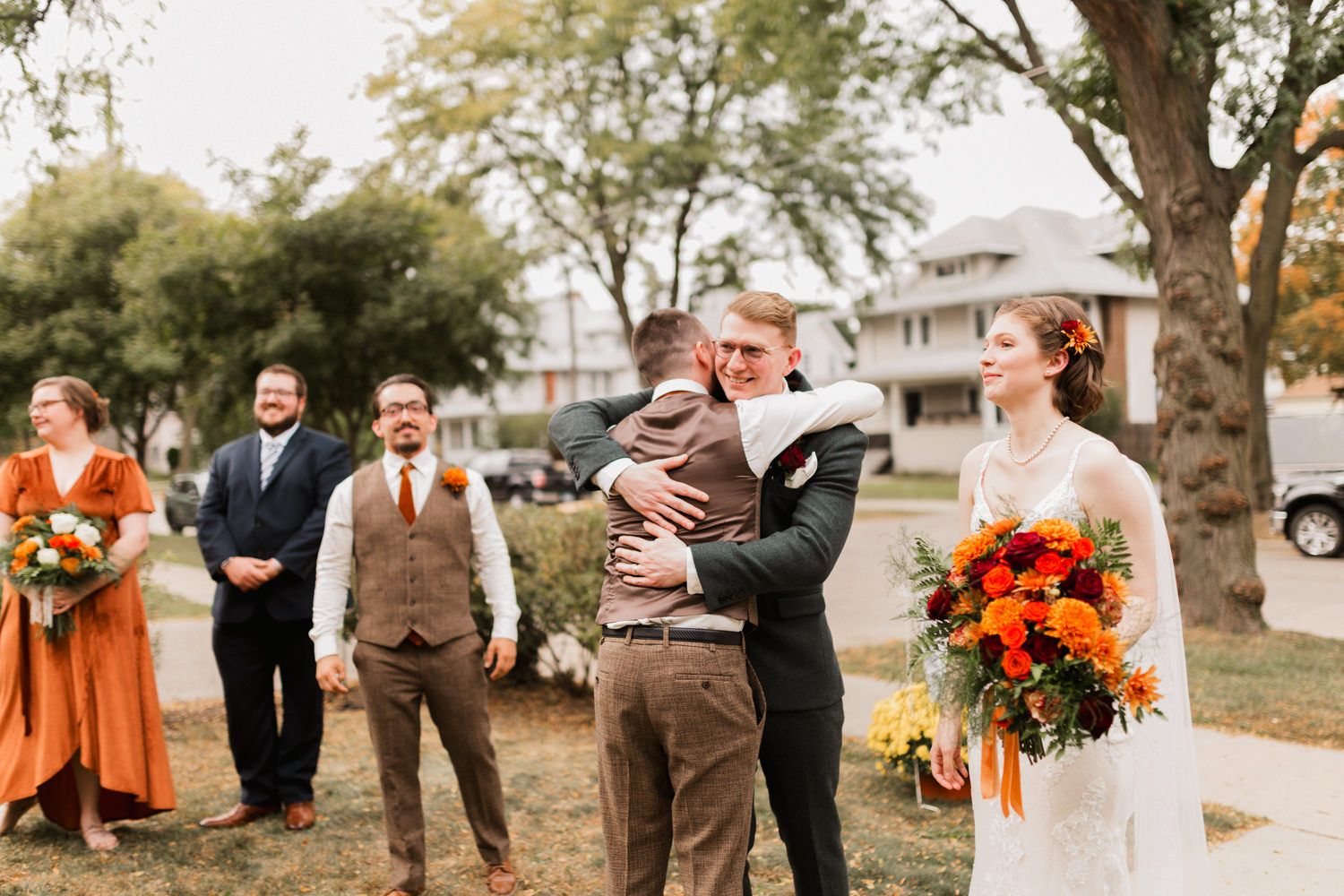 Outdoor fall wedding ceremony with bridesmaids in orange dresses and autumn-colored floral bouquets.