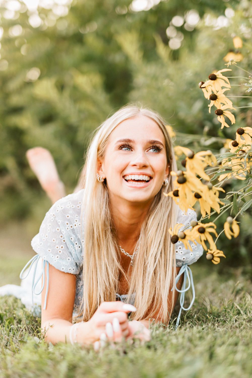 Candid laughing portrait in blue dress with bokeh and yellow flowers.