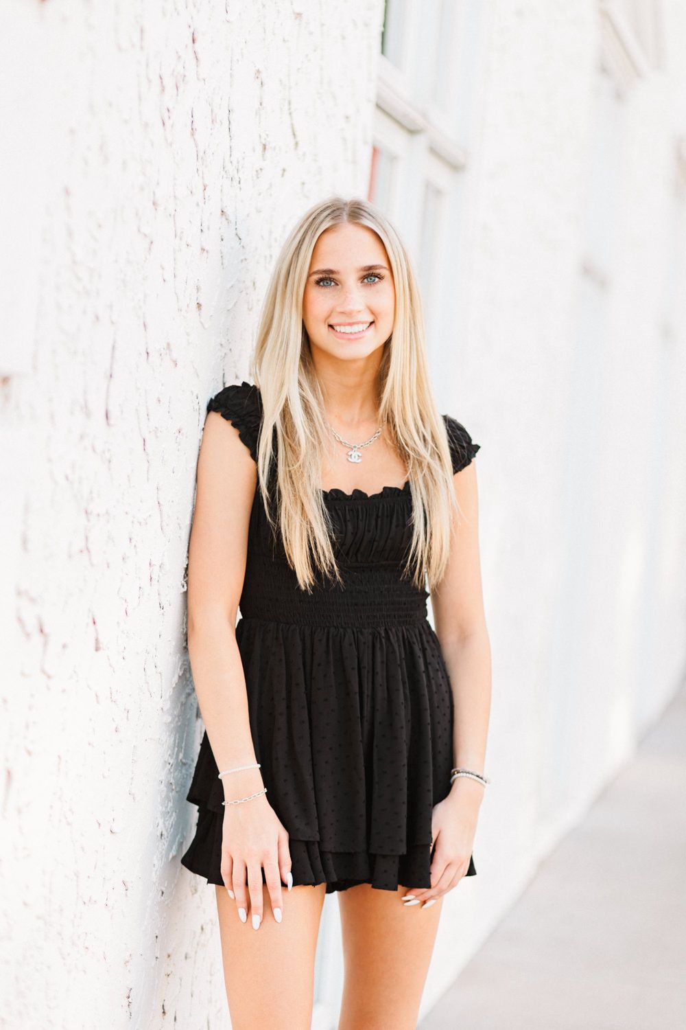 Casual fashion shoot against white textured wall featuring black summer dress.