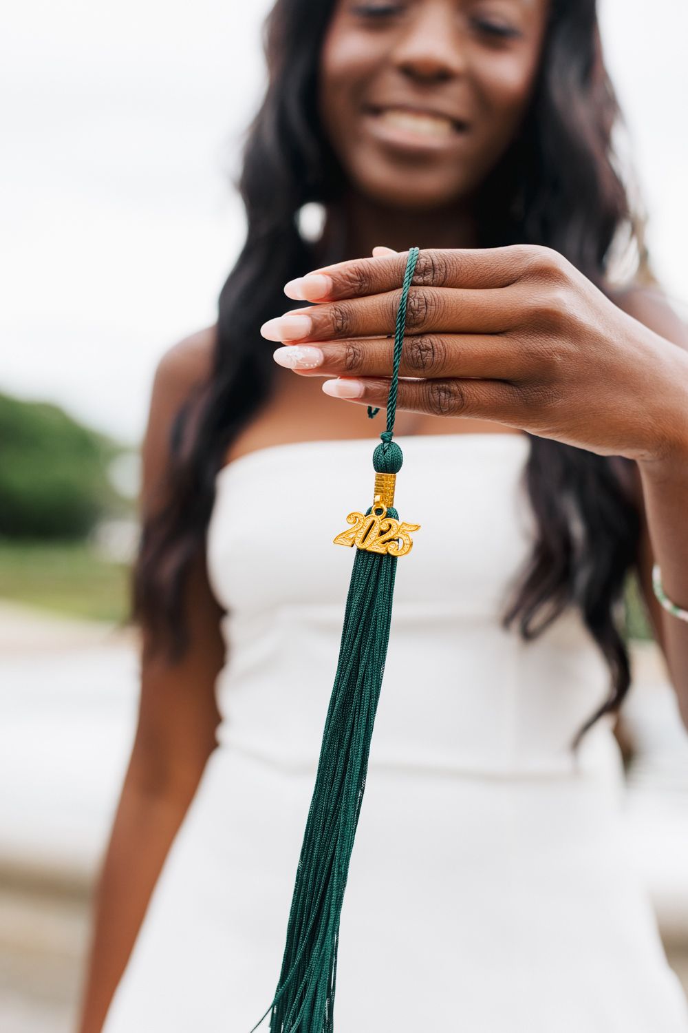 Close-up shots of hands holding green and gold graduation tassel.
