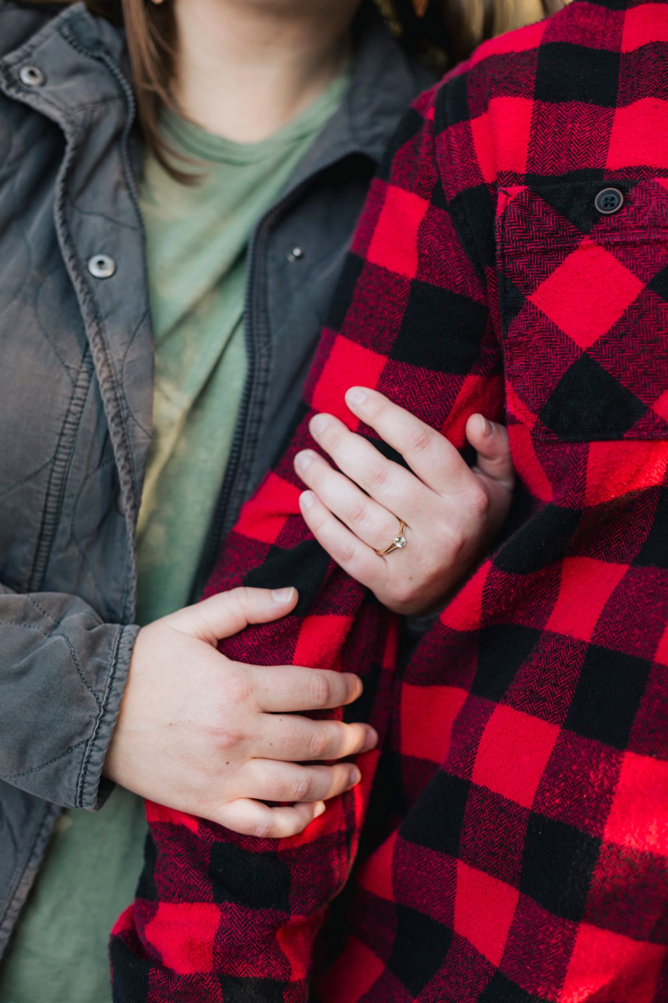 Close up of engaged hands holding onto a red and black buffalo plaid flannel jacket sleeve.