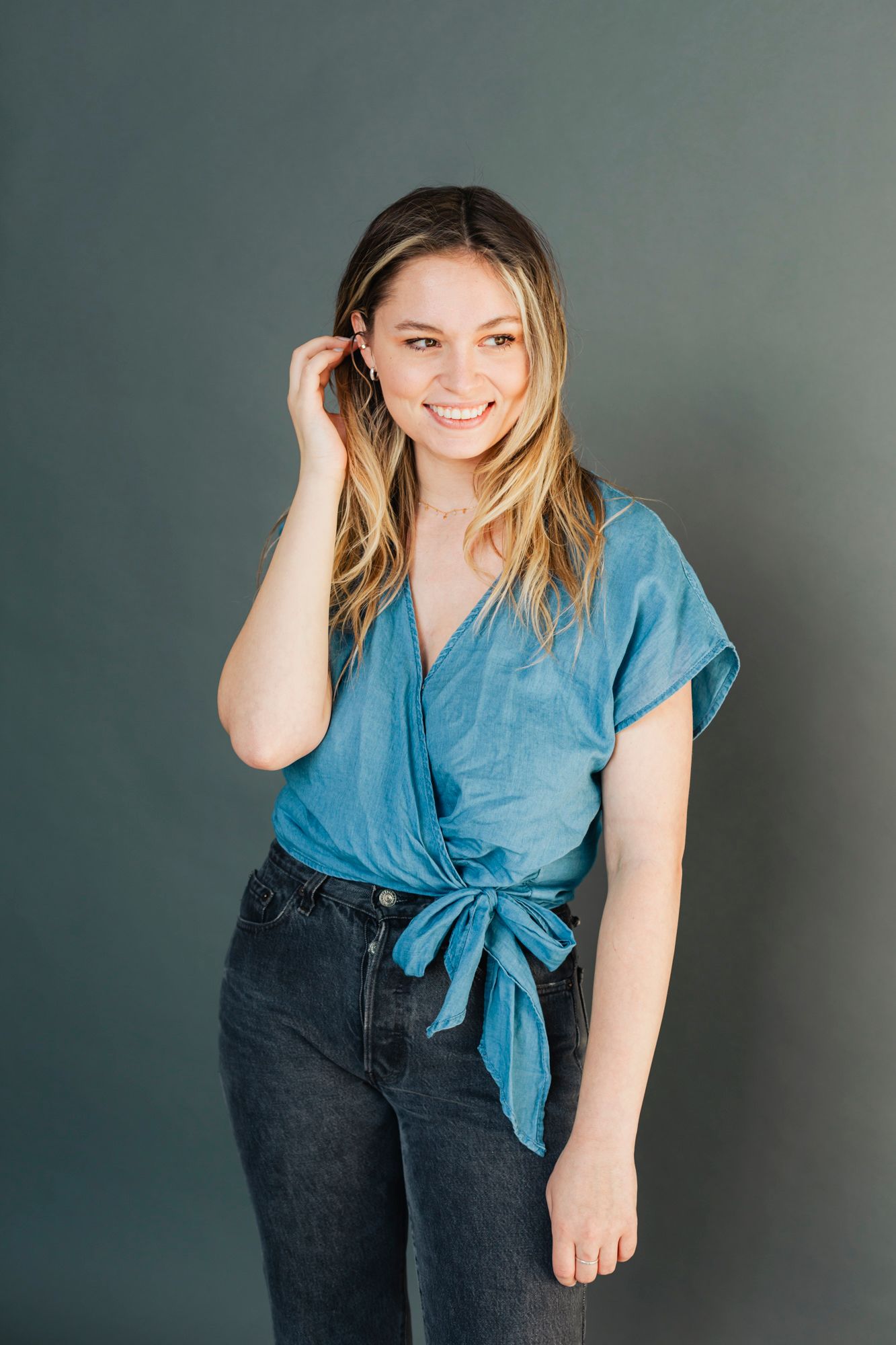 Casual portrait of person in blue wrap top and jeans against teal background.