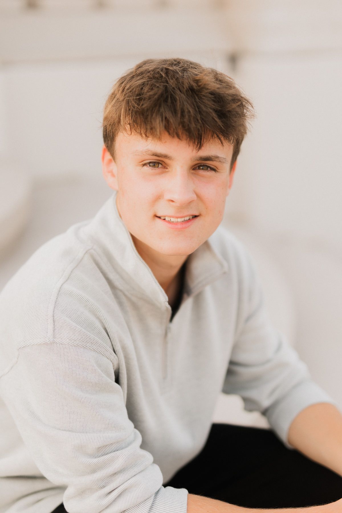 Smiling teenage boy in gray quarter-zip sweatshirt posing for casual portrait outdoors.