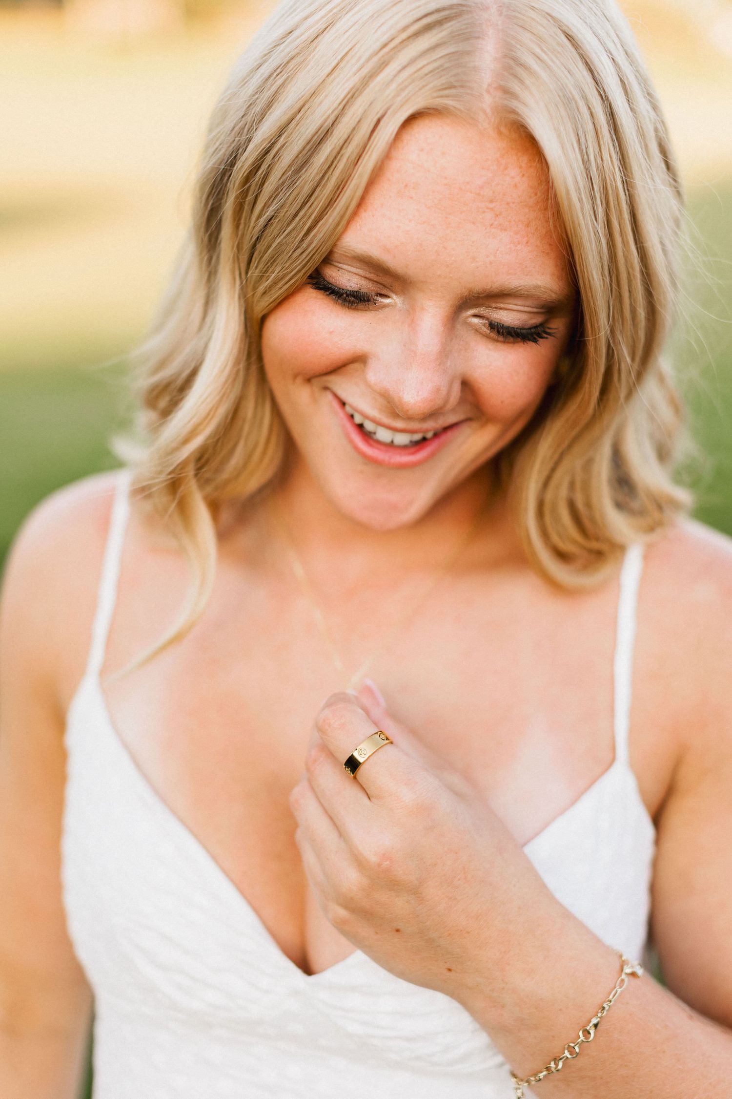 Close-up portrait showing a joyful smile and engagement ring against a warm outdoor background.