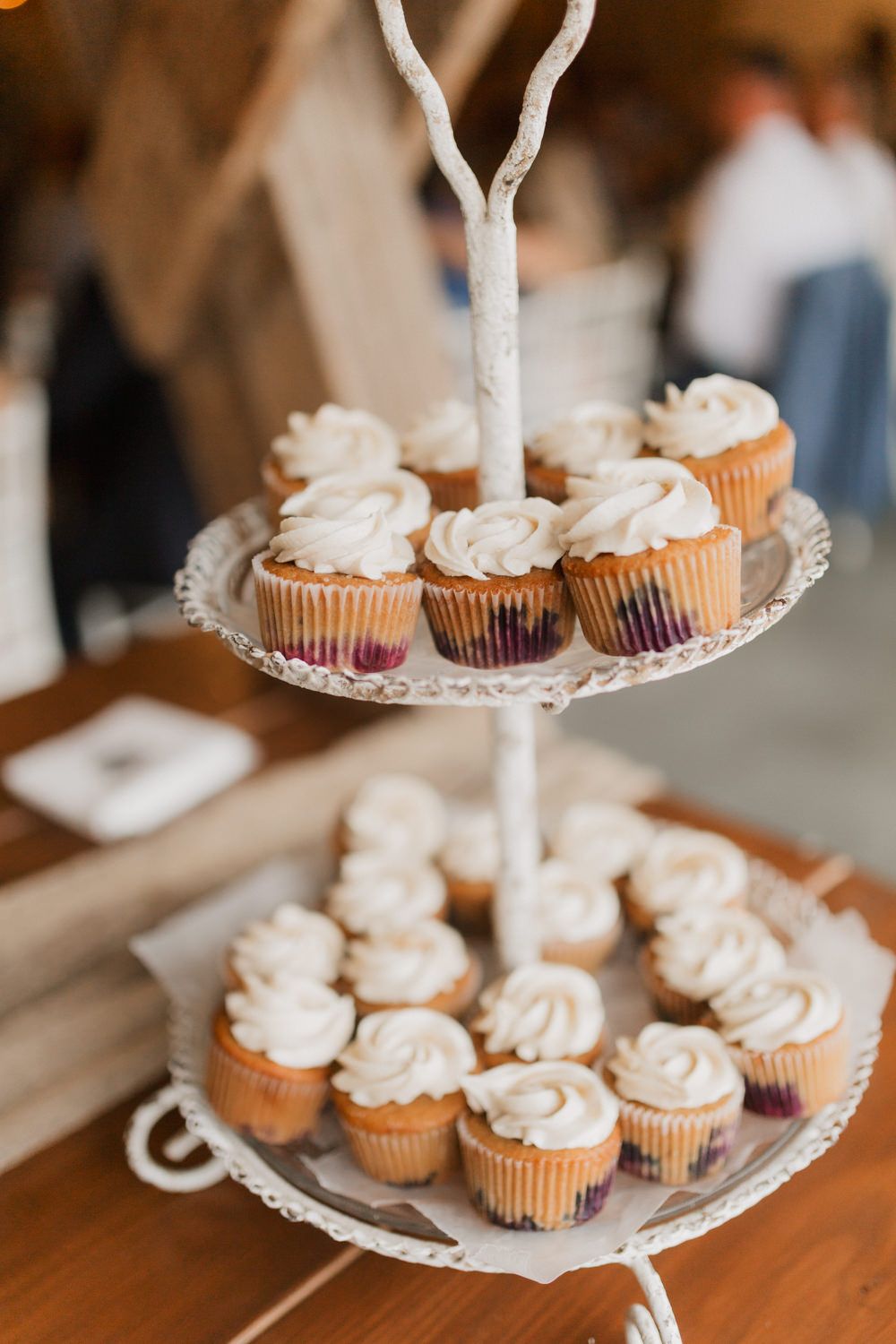 Tiered display of white frosted cupcakes on an elegant serving stand at a wedding reception.