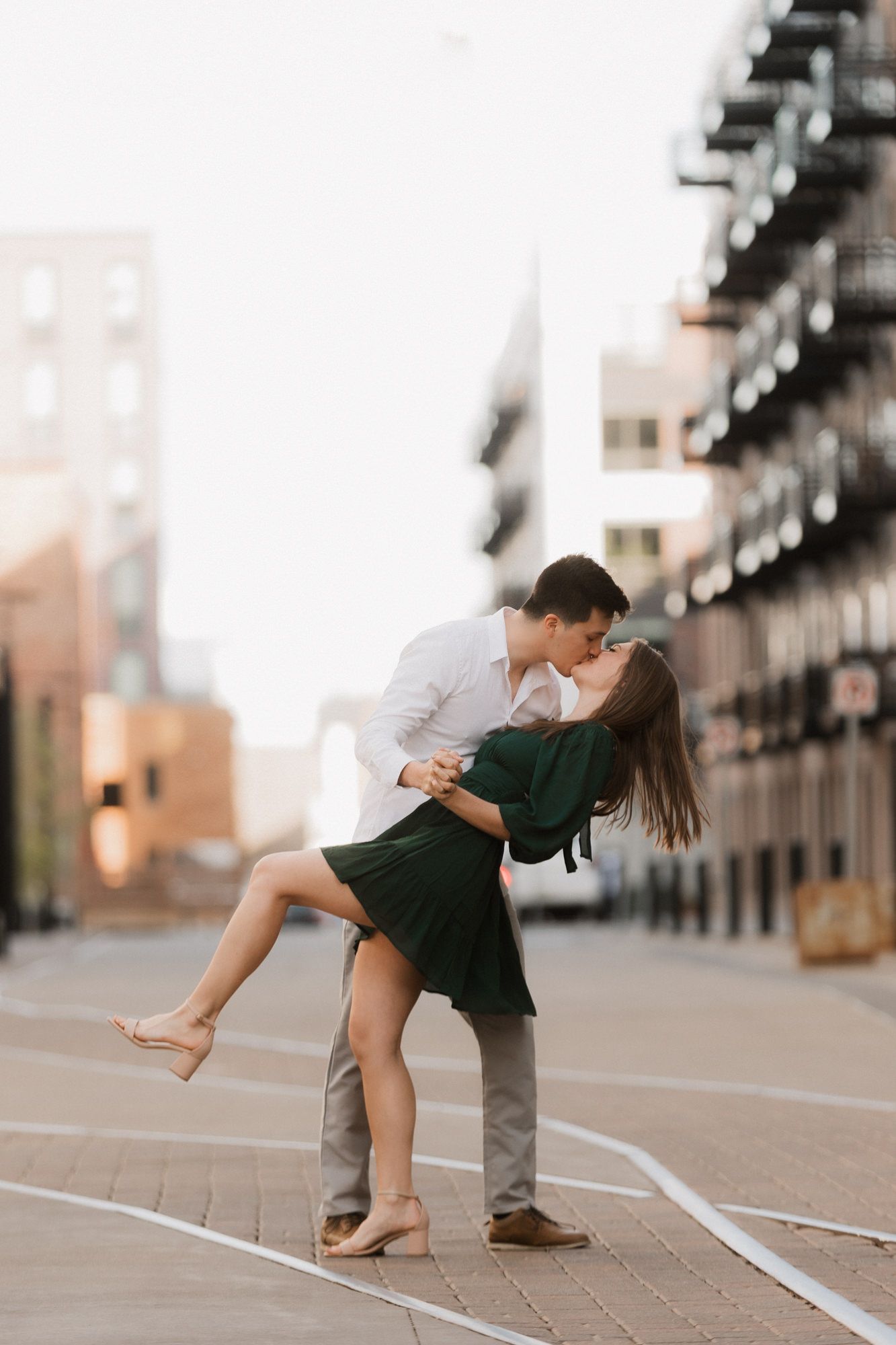 Couple sharing a romantic dip kiss on an urban street at golden hour in city setting.