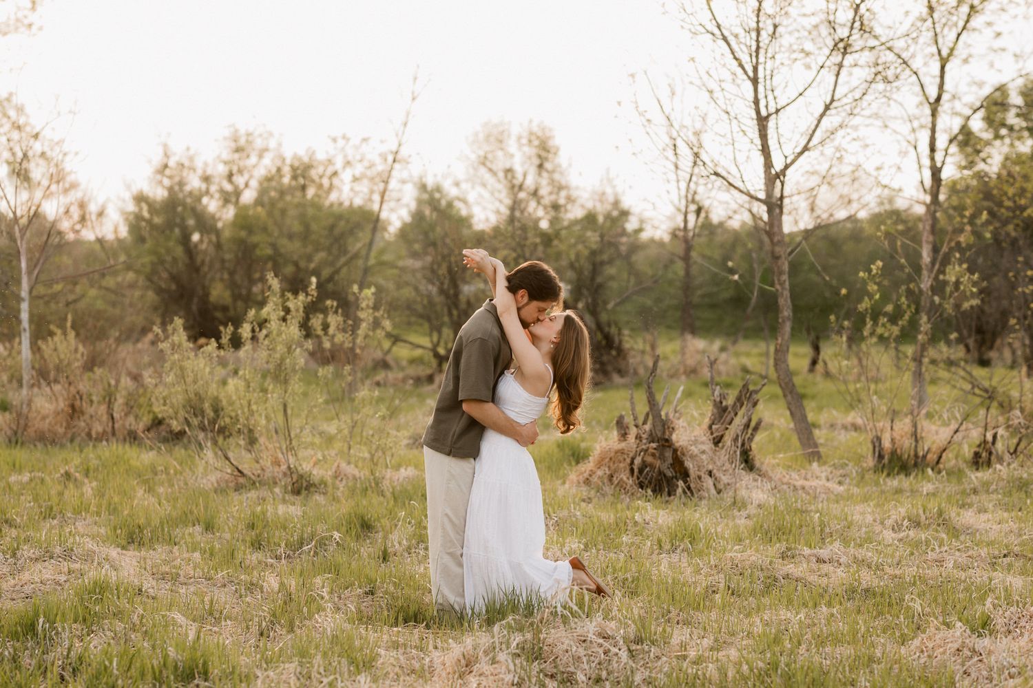 Couple sharing a tender embrace in a sunlit meadow during golden hour engagement photoshoot.