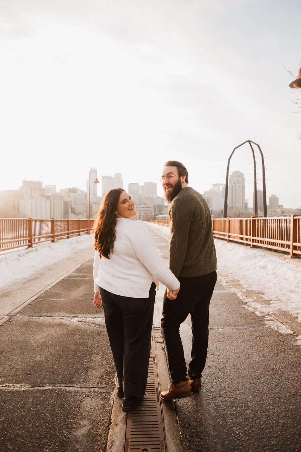 A couple shares a romantic moment on a bridge with a city skyline visible in the background.