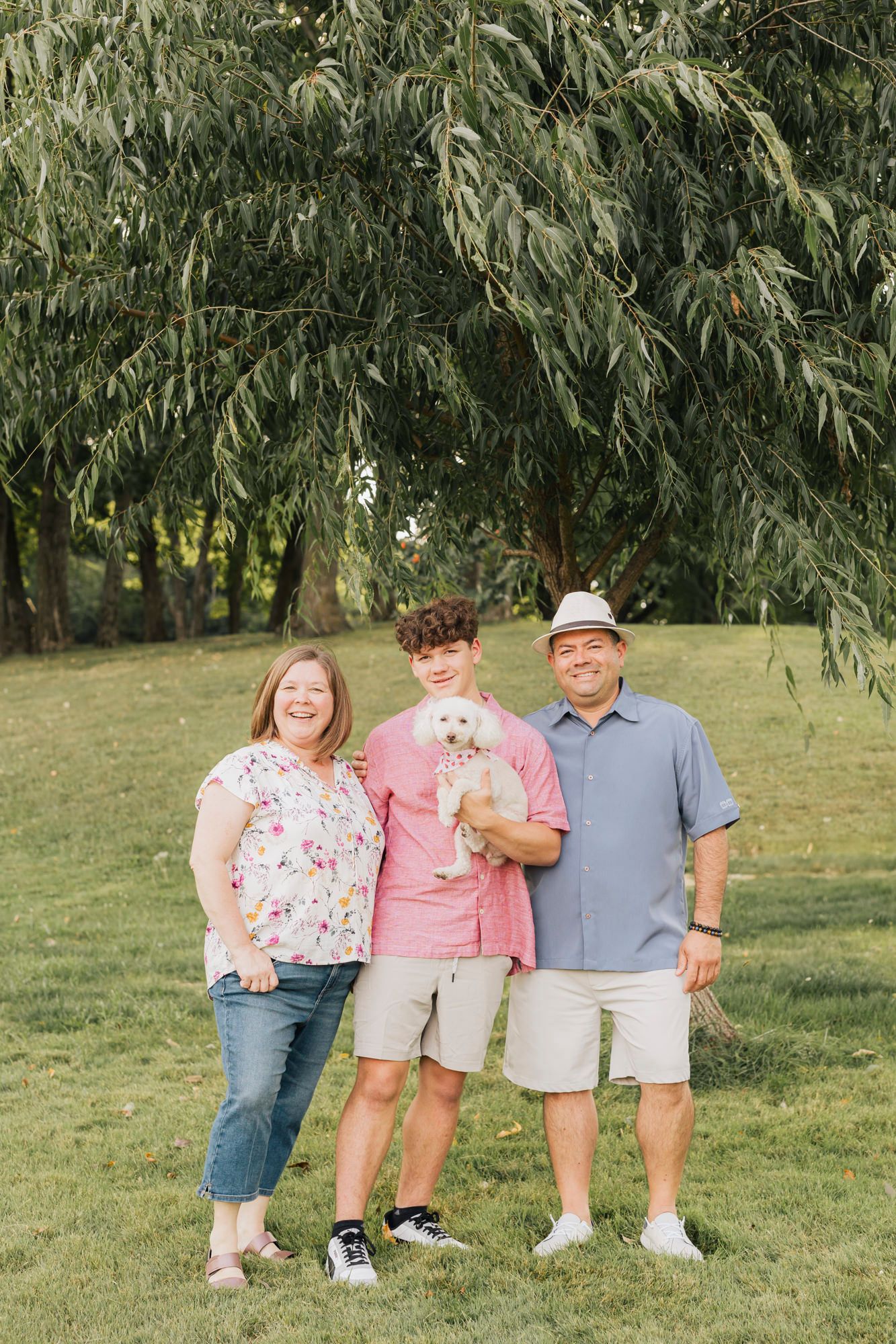 Small family group walks together through a grassy area with willow trees in background.