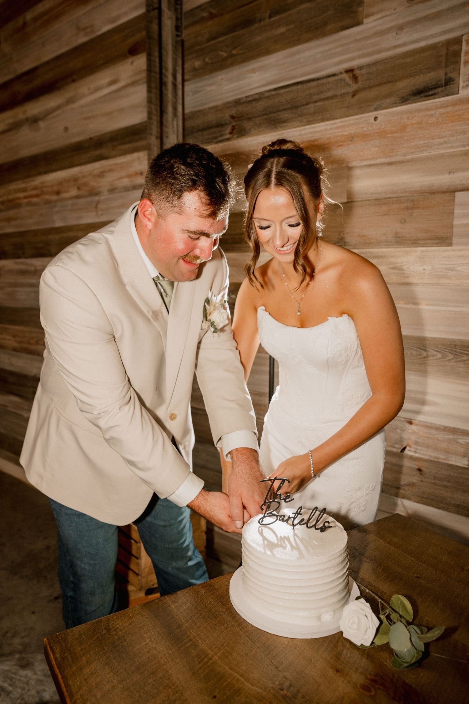 Bride and groom cutting white tiered wedding cake in rustic barn venue.