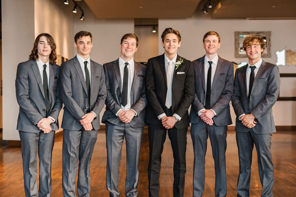 Wide shot of wedding party members lined up in matching formal attire against neutral background.