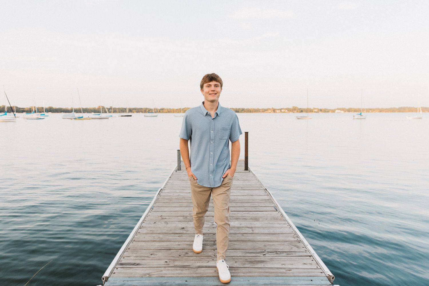 Figure walking on wooden dock over blue water at sunset.
