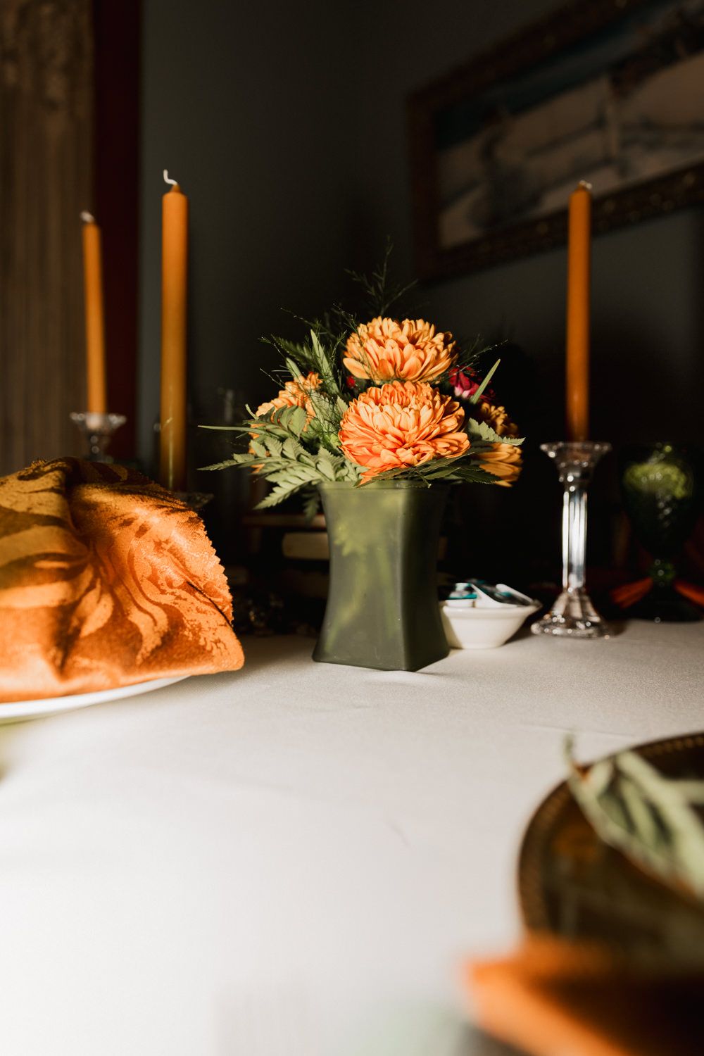 Orange floral centerpiece with tall white candles on an elegant table setting.