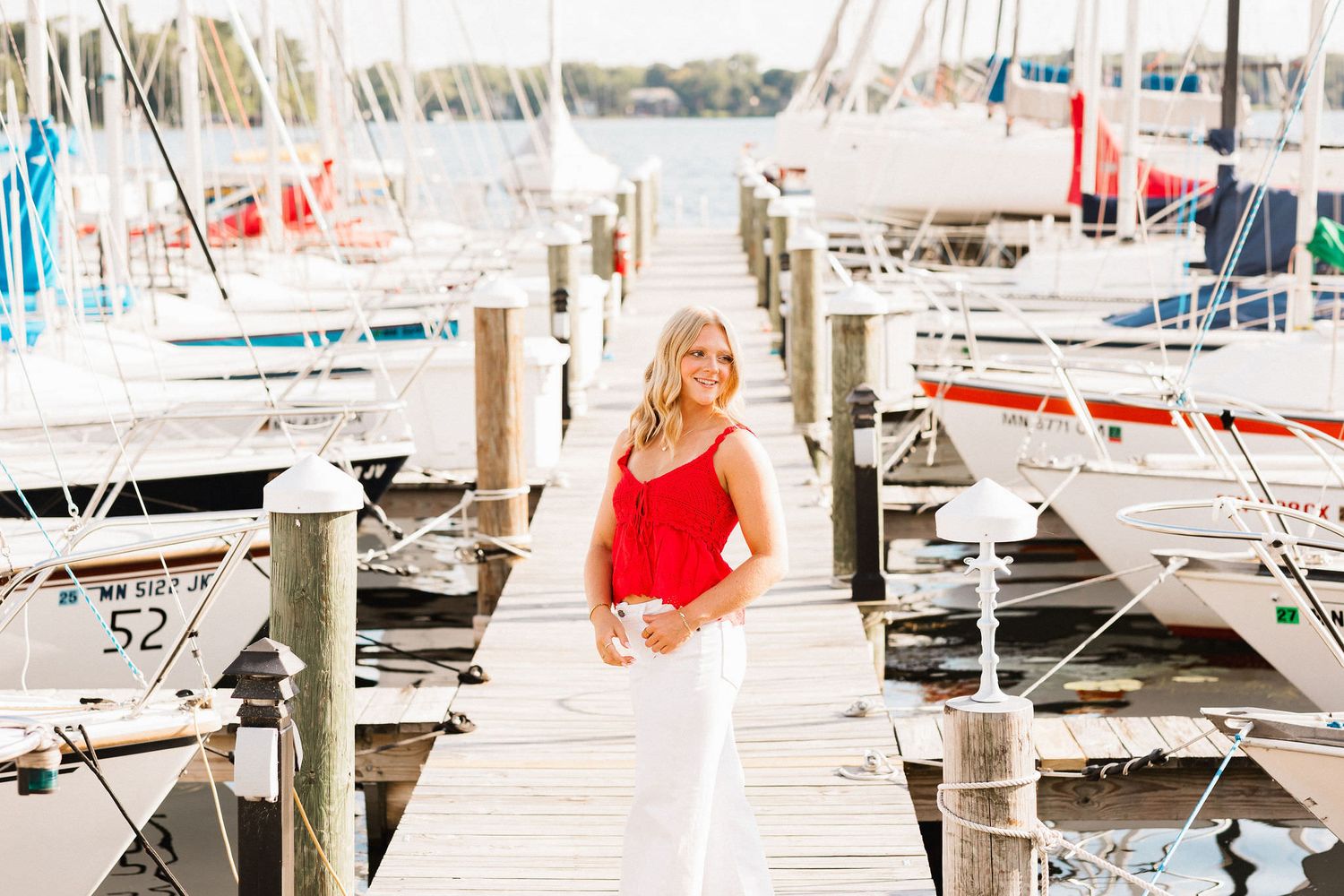 A wooden dock lined with sailboats and yachts at a marina on a sunny summer day.