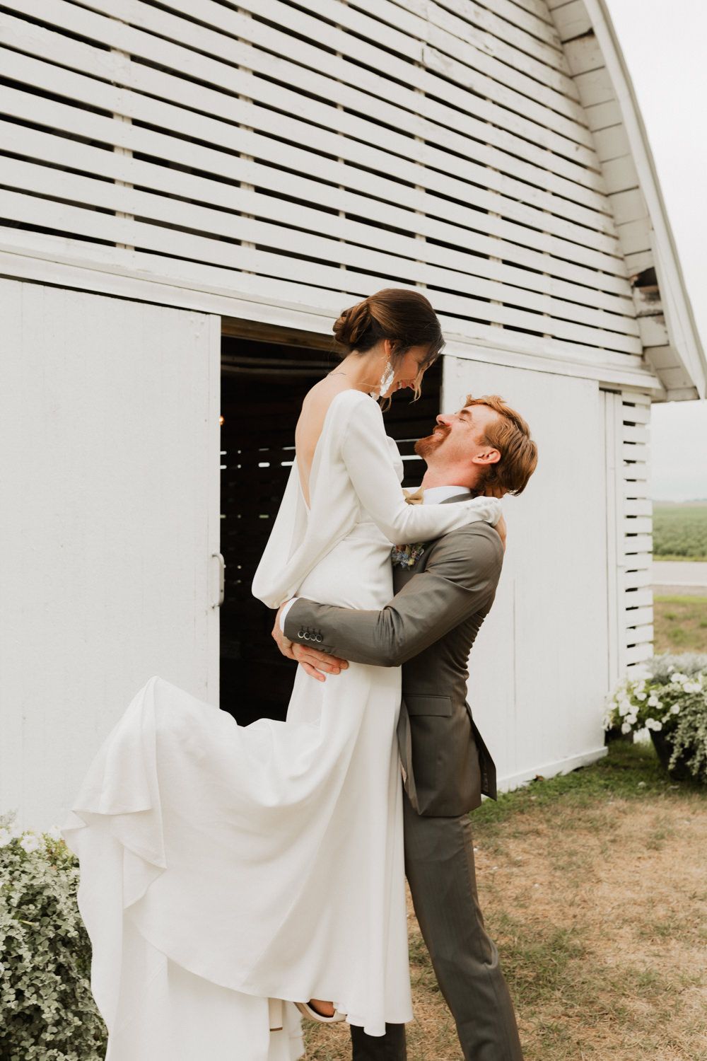 A couple sharing a romantic moment against a white barn backdrop during their wedding.