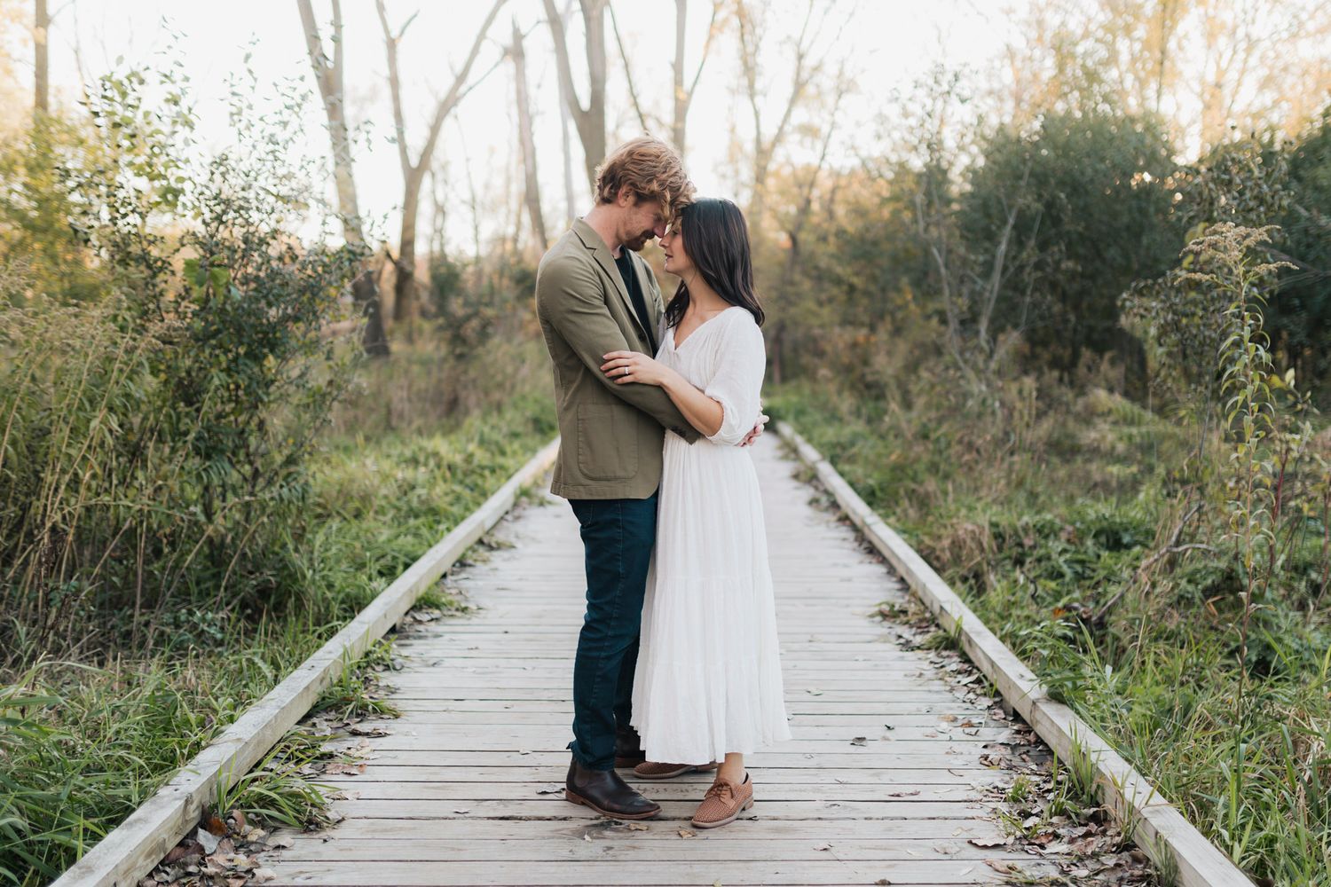 A romantic couple embraces on a wooden boardwalk surrounded by autumn foliage.
