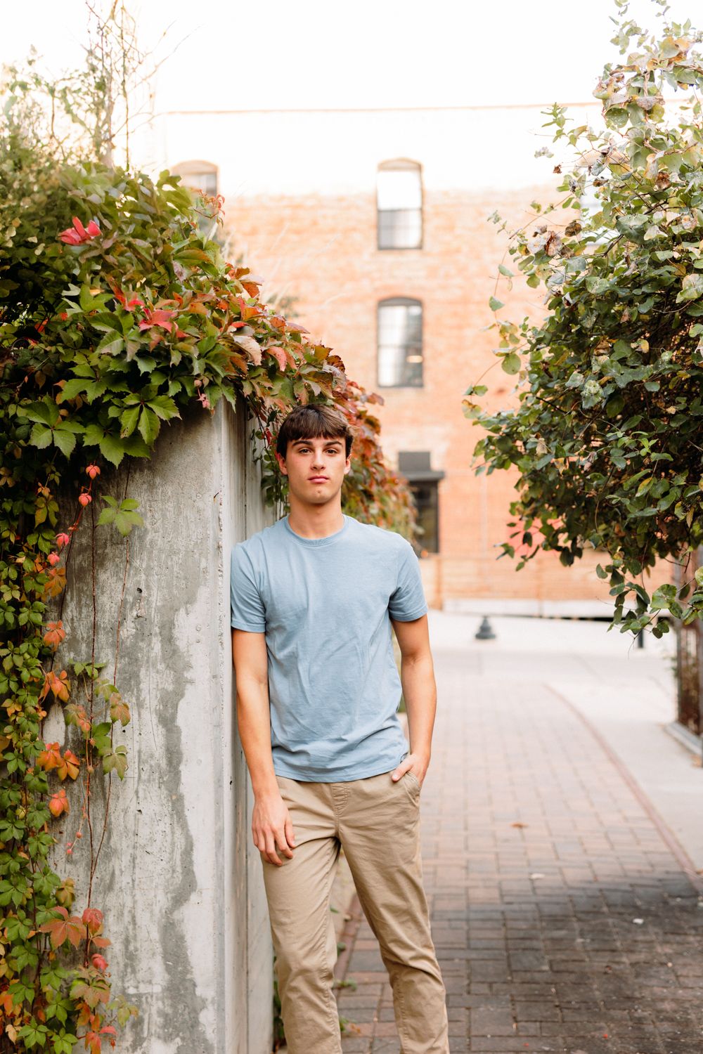 A casual portrait series against a brick wall with flowering bushes and greenery.