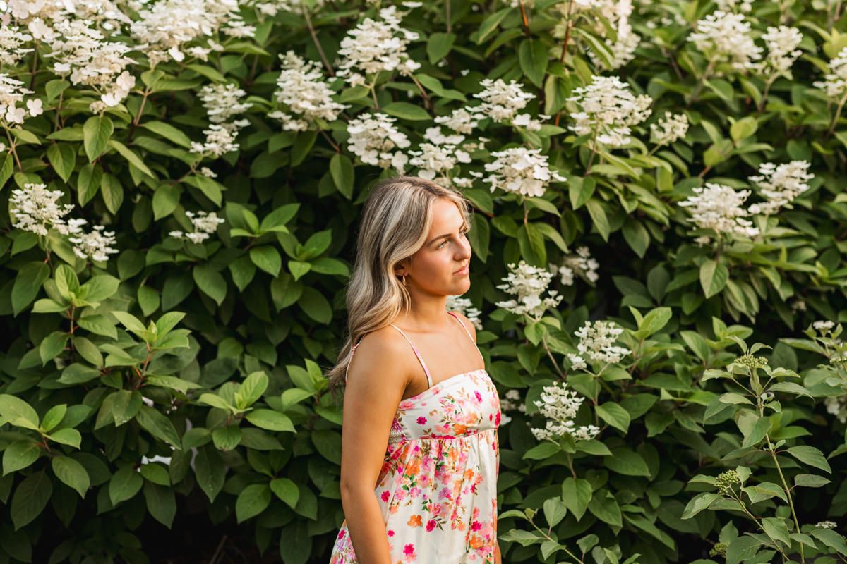 Feminine summer outfit worn against a backdrop of blooming white hydrangea bushes in a garden setting.
