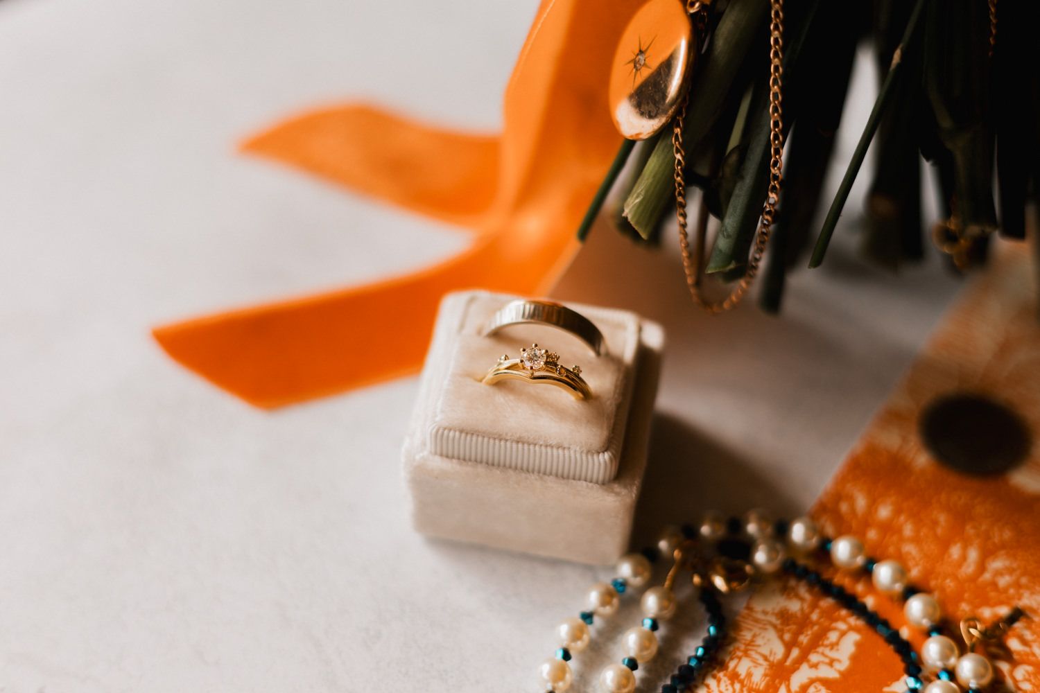 Decorative orange velvet ribbon with gold hardware and pearl embellishments displayed on a neutral background.