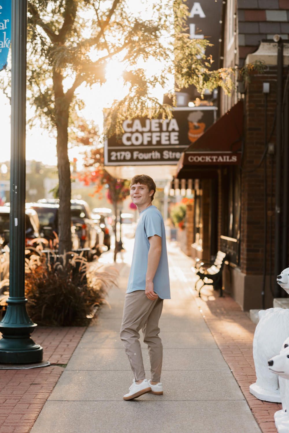 A golden sunset illuminates a brick-paved sidewalk with shops and trees along a downtown street.