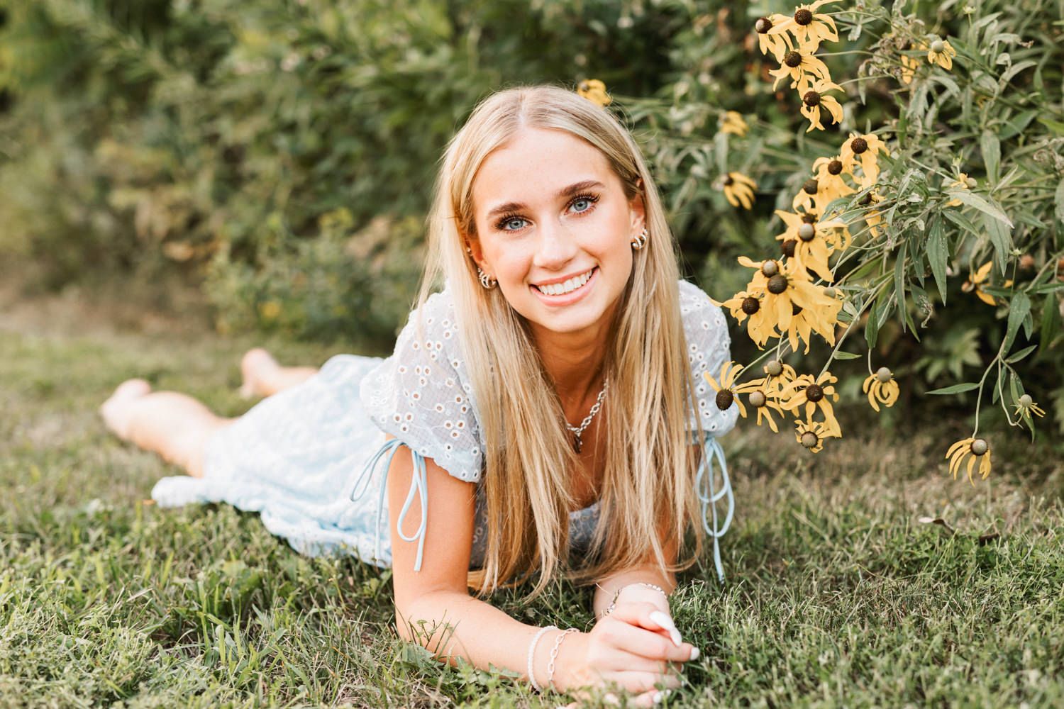 Summer portrait laying in grass wearing light blue dress near yellow flowers.