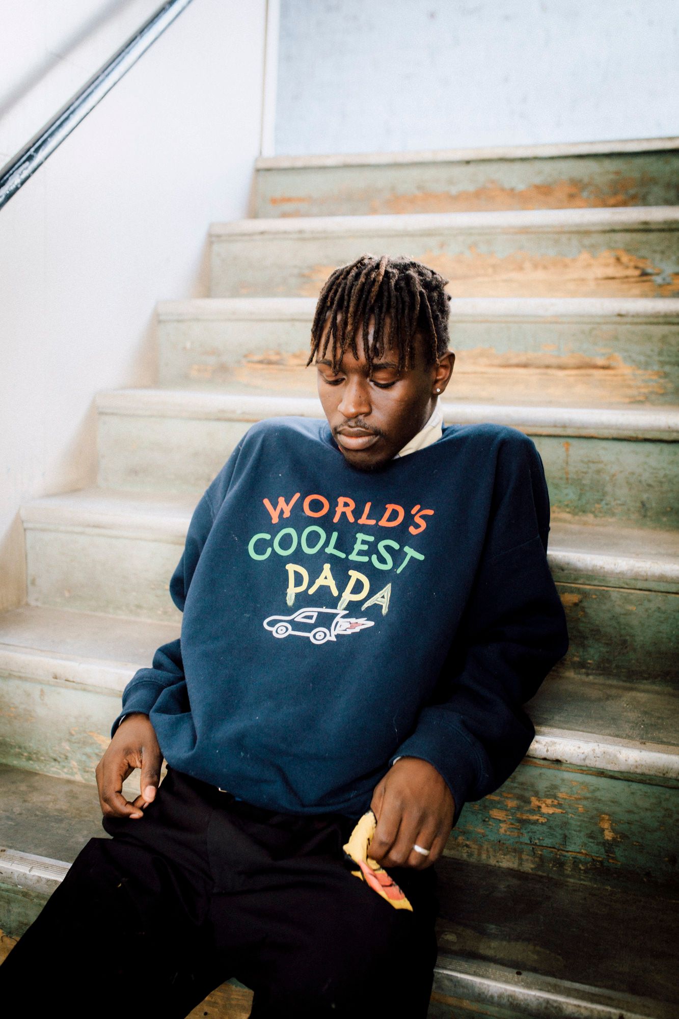 Person wearing a 'World's Coolest Papa' sweatshirt sitting on concrete stairs.