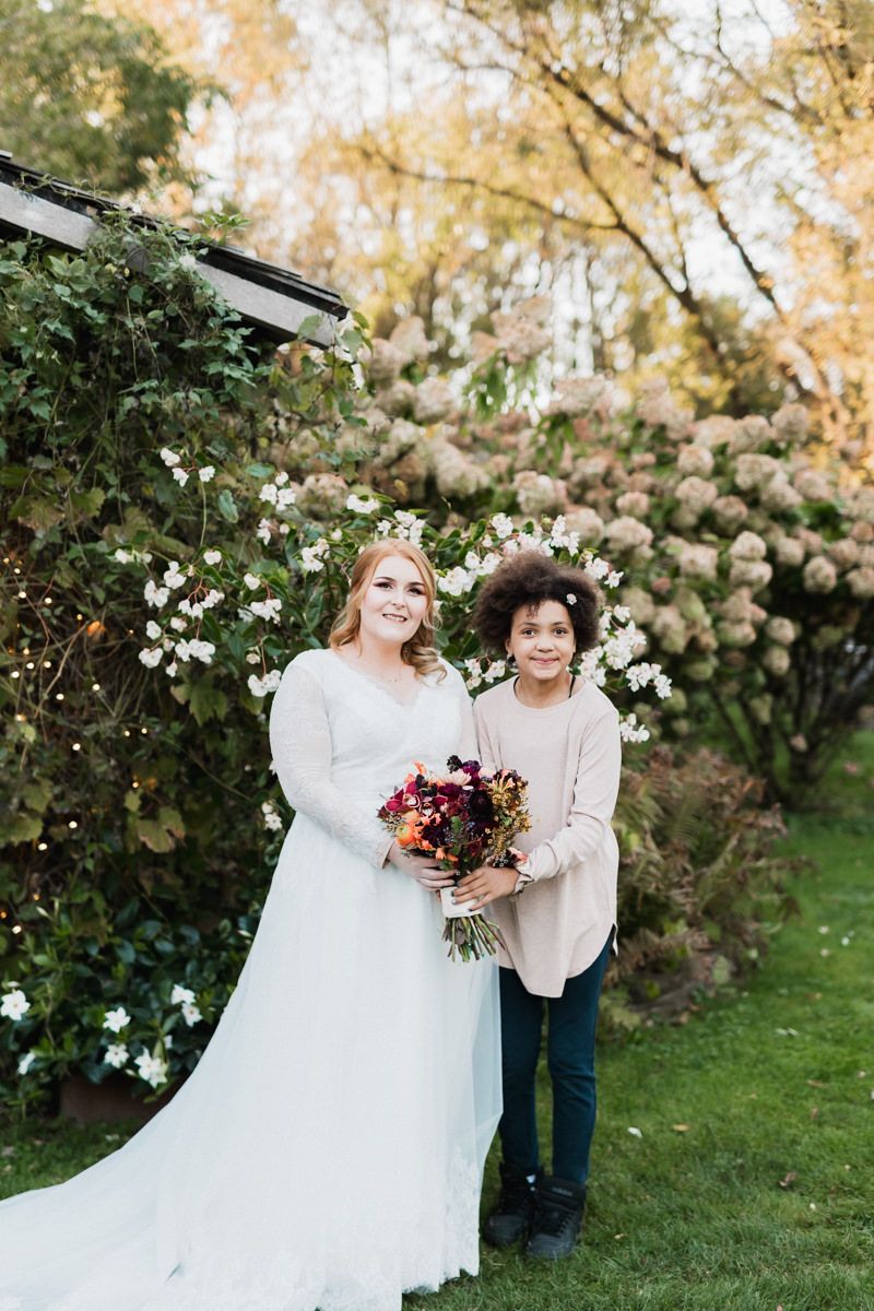 A joyful moment captured in a garden with blooming white flowers and autumn foliage.