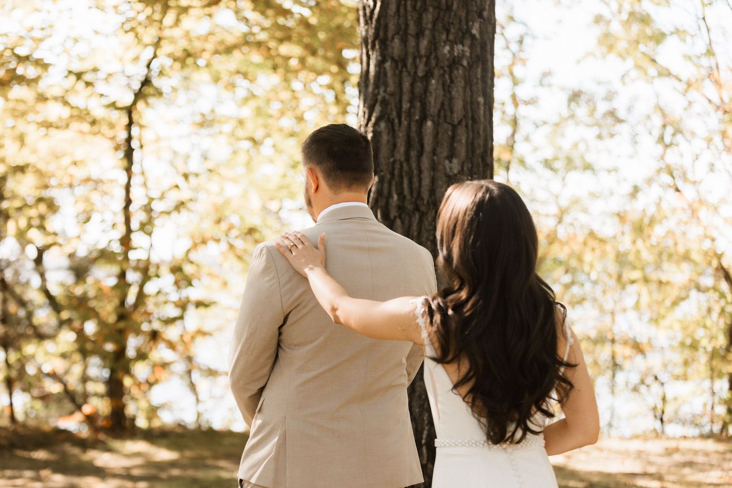 A couple shares an intimate moment while walking through a sunlit autumn forest.