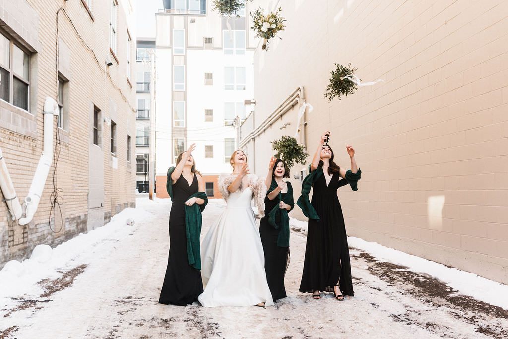 Wedding party poses playfully in an outdoor alley with light colored walls.