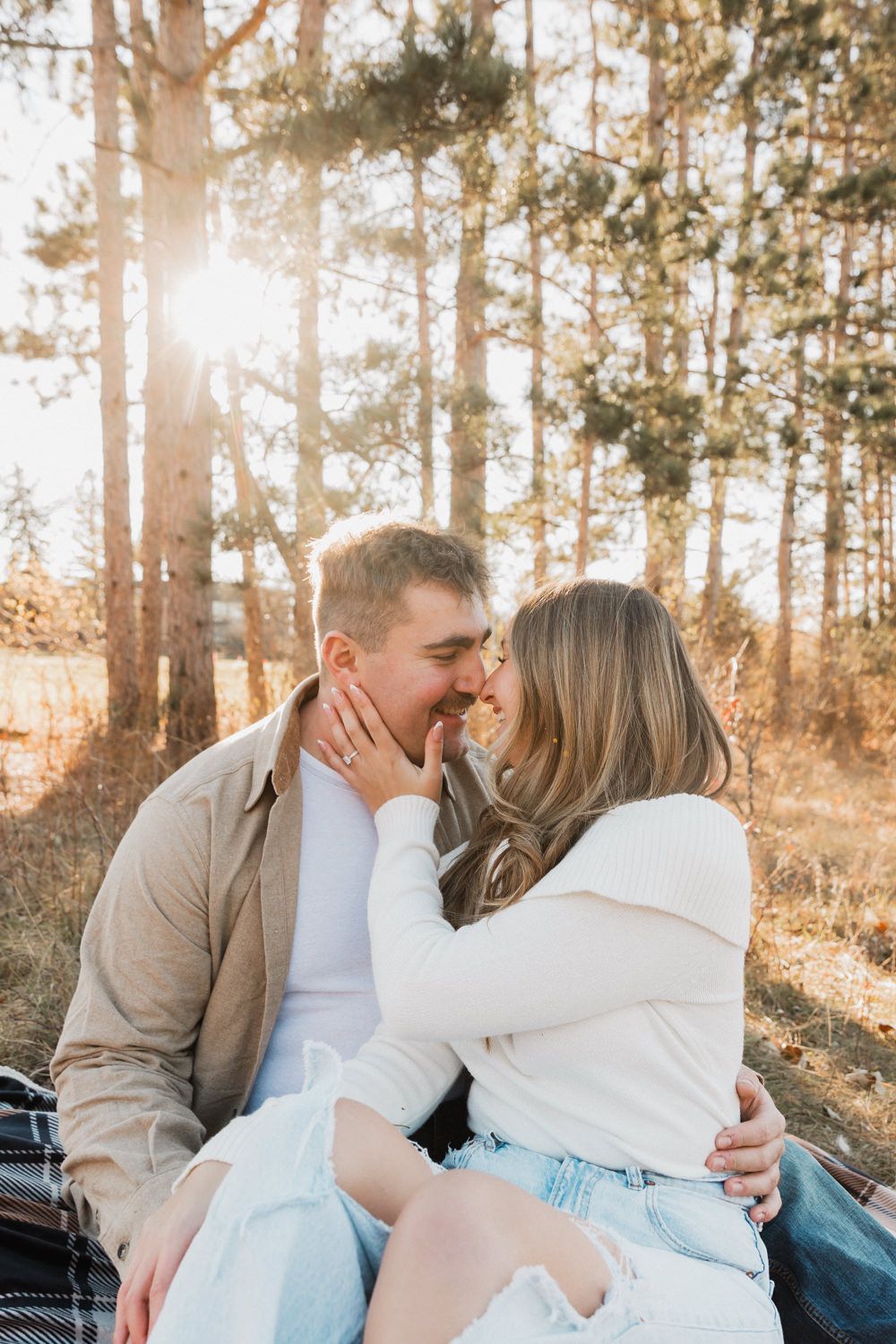 A tender moment captured between a couple sitting together in a wooded area during golden hour.