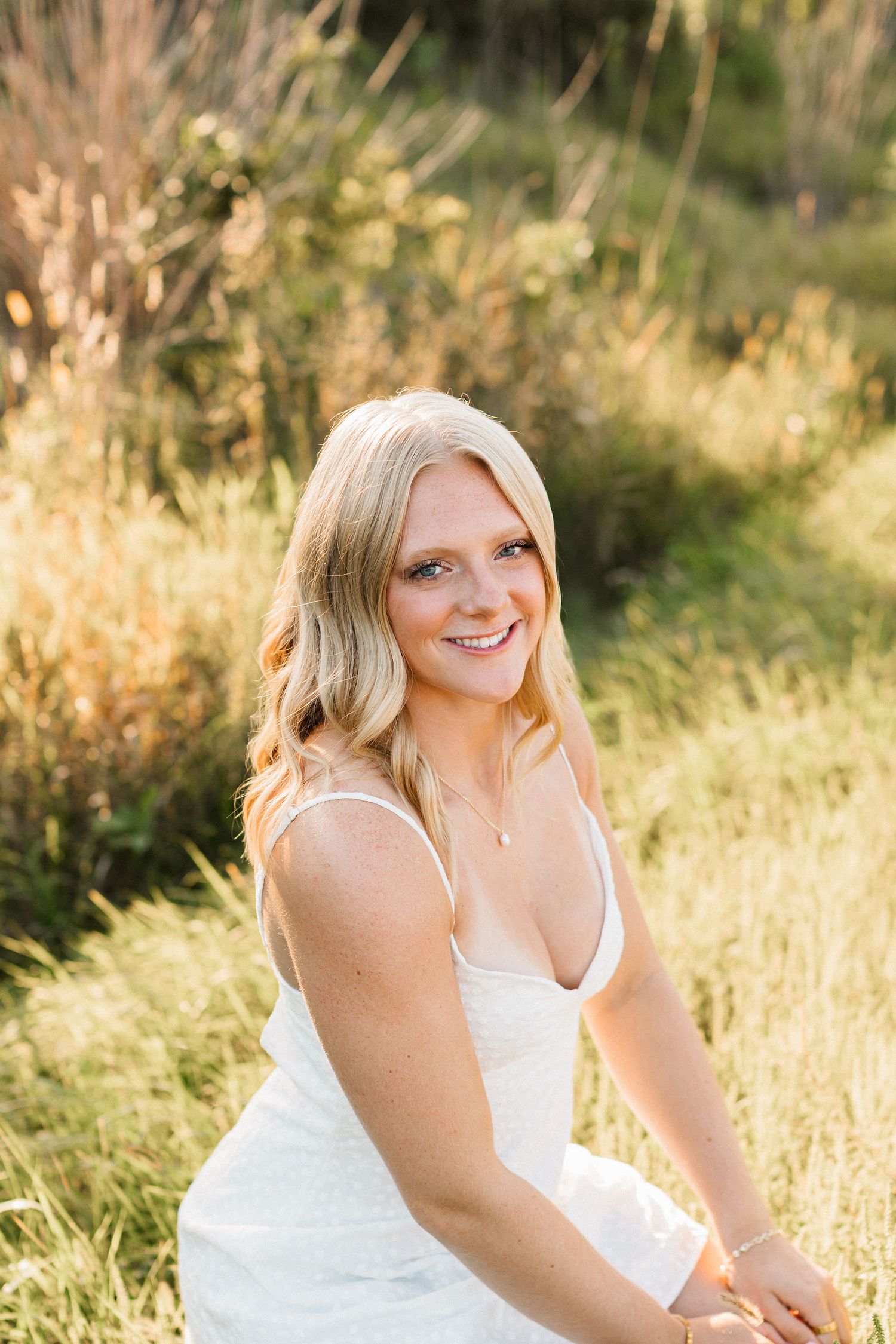Woman in white dress smiles during outdoor summer photoshoot with golden light.