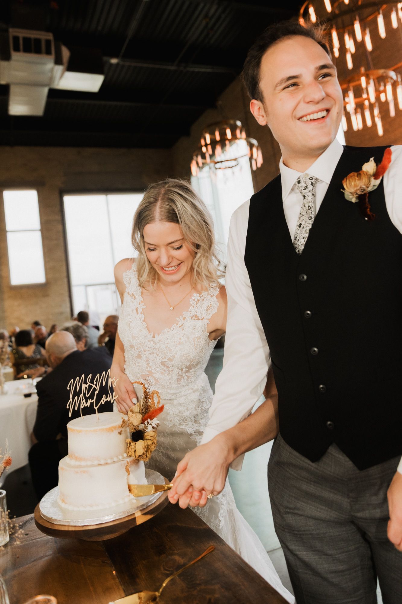 Smiling bride and groom cutting their white wedding cake together at a modern indoor reception venue.