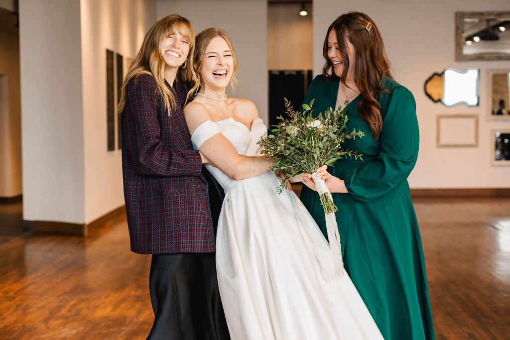 Candid wedding party photo showing joyful moments between bridesmaids in an indoor venue.