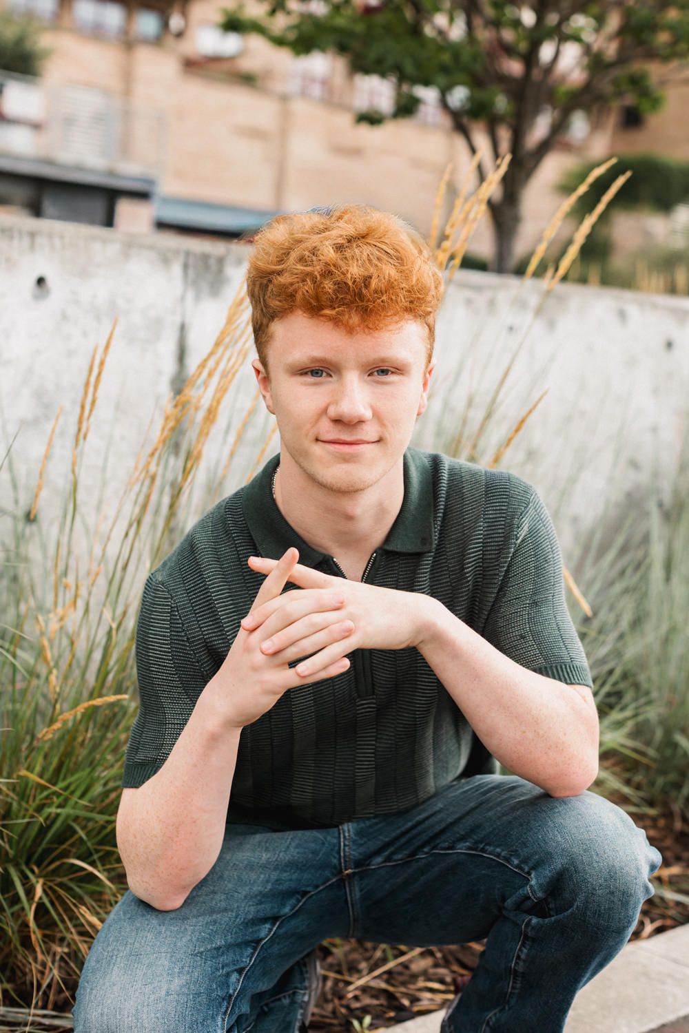 Young person in dark sweater sitting outdoors against ornamental grasses in natural light.