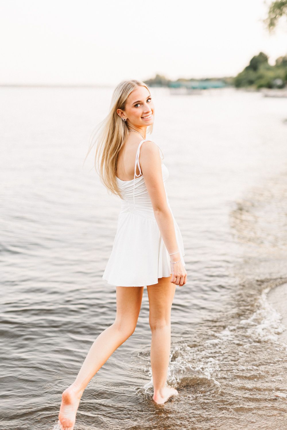 Carefree summer pose at beach shoreline in white sundress.