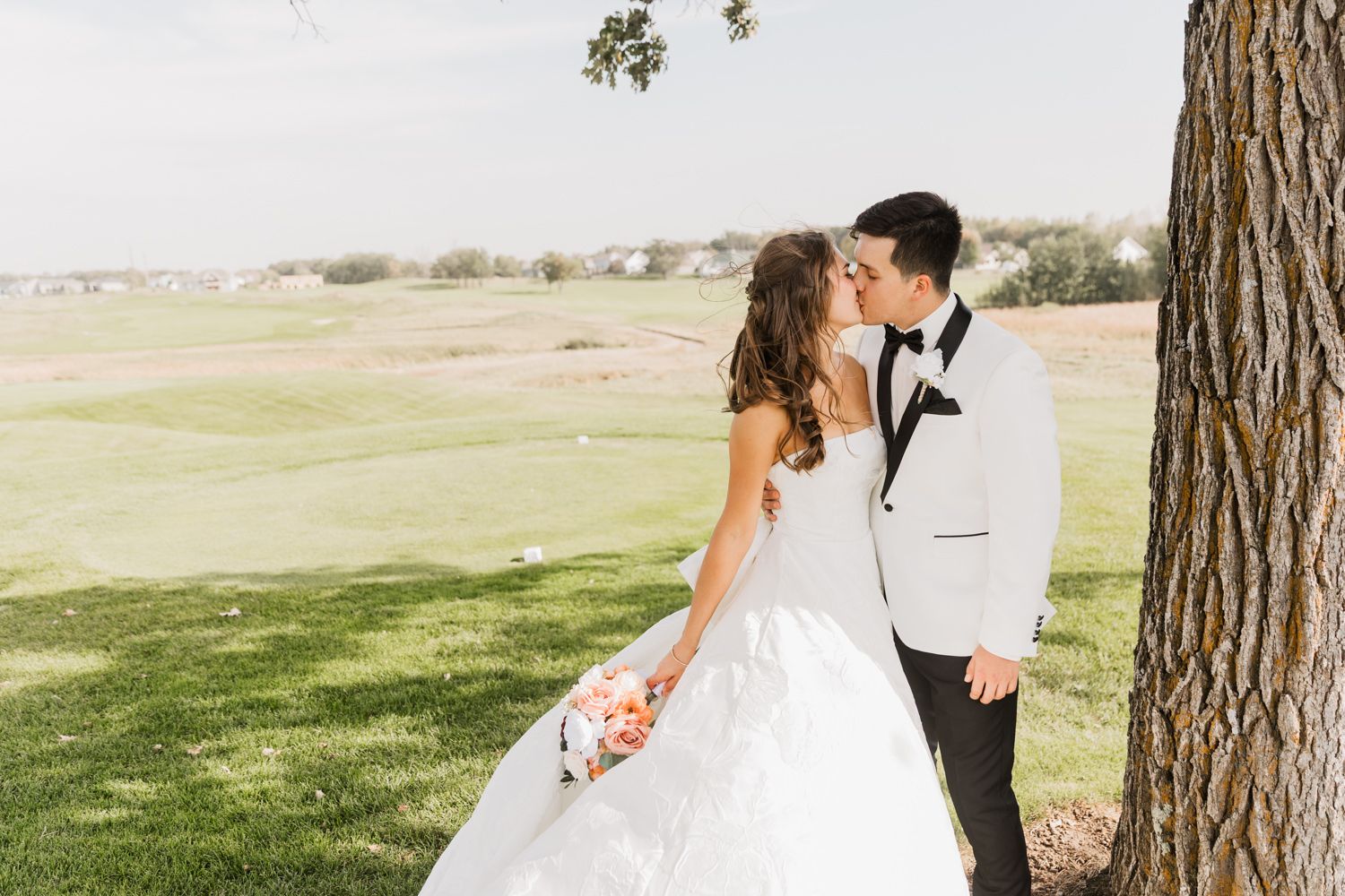 A romantic wedding couple poses for photos under tall pine trees in a scenic outdoor setting.