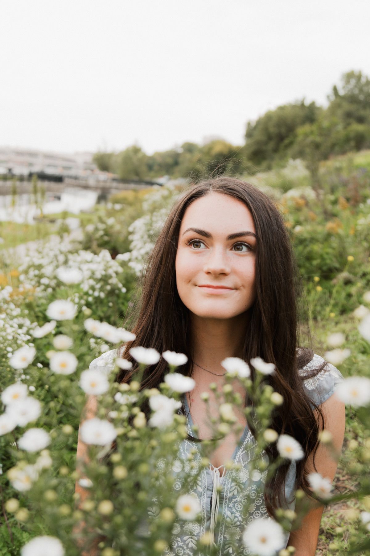 Young woman with long dark hair smiling in a wildflower field with white blooms in the foreground.