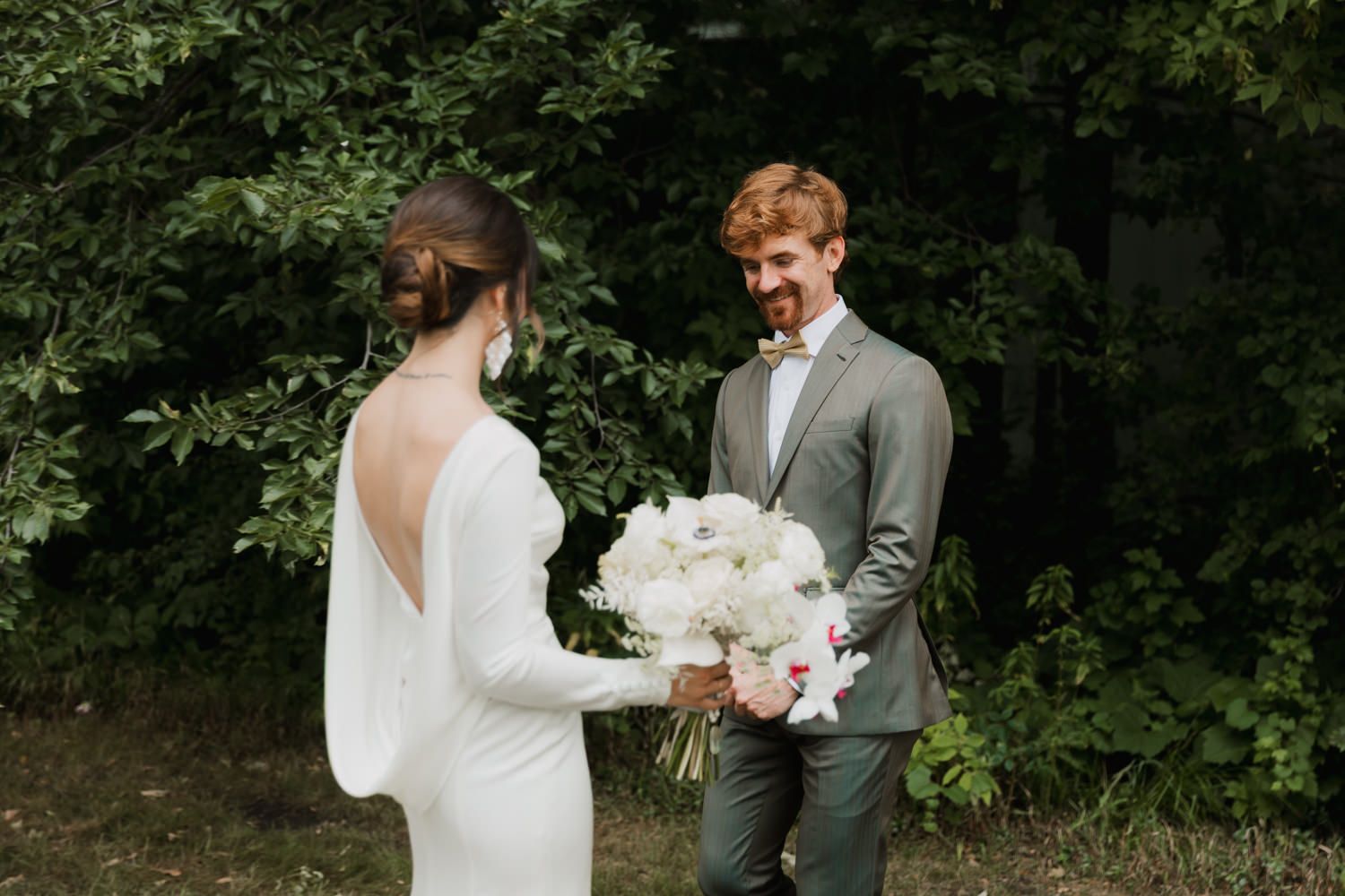 A romantic wedding moment captured outdoors with a backlit couple and lush greenery in the background.