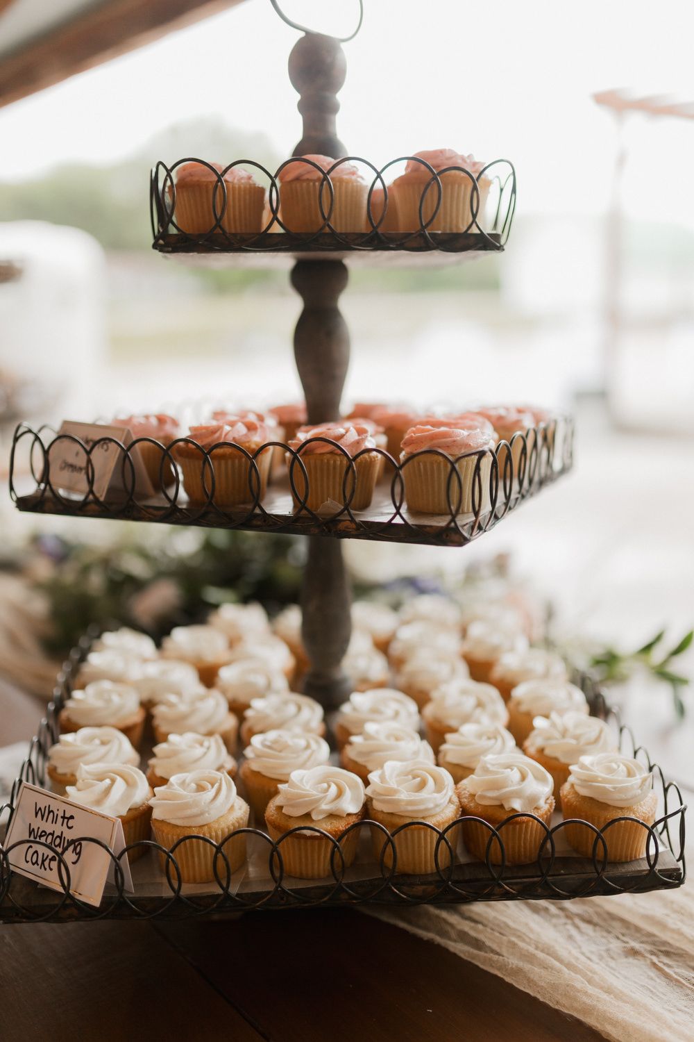 Tiered display of white frosted cupcakes arranged on dark metal stands at a wedding reception.