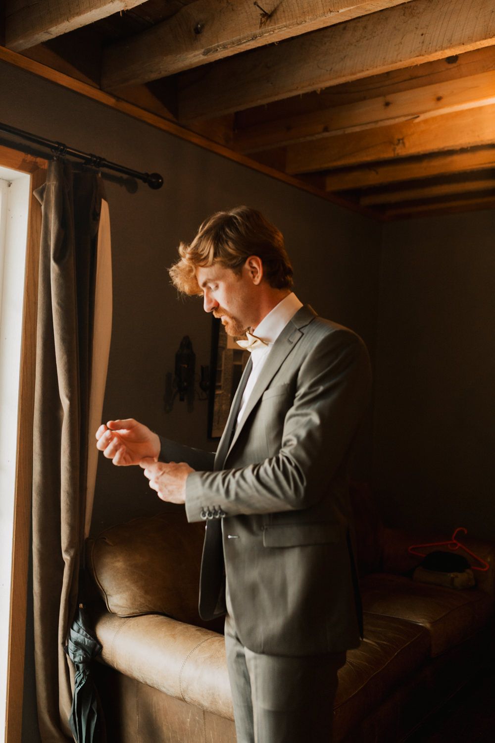 Moody getting-ready scene in dark wood room with figure adjusting tie in warm lighting.