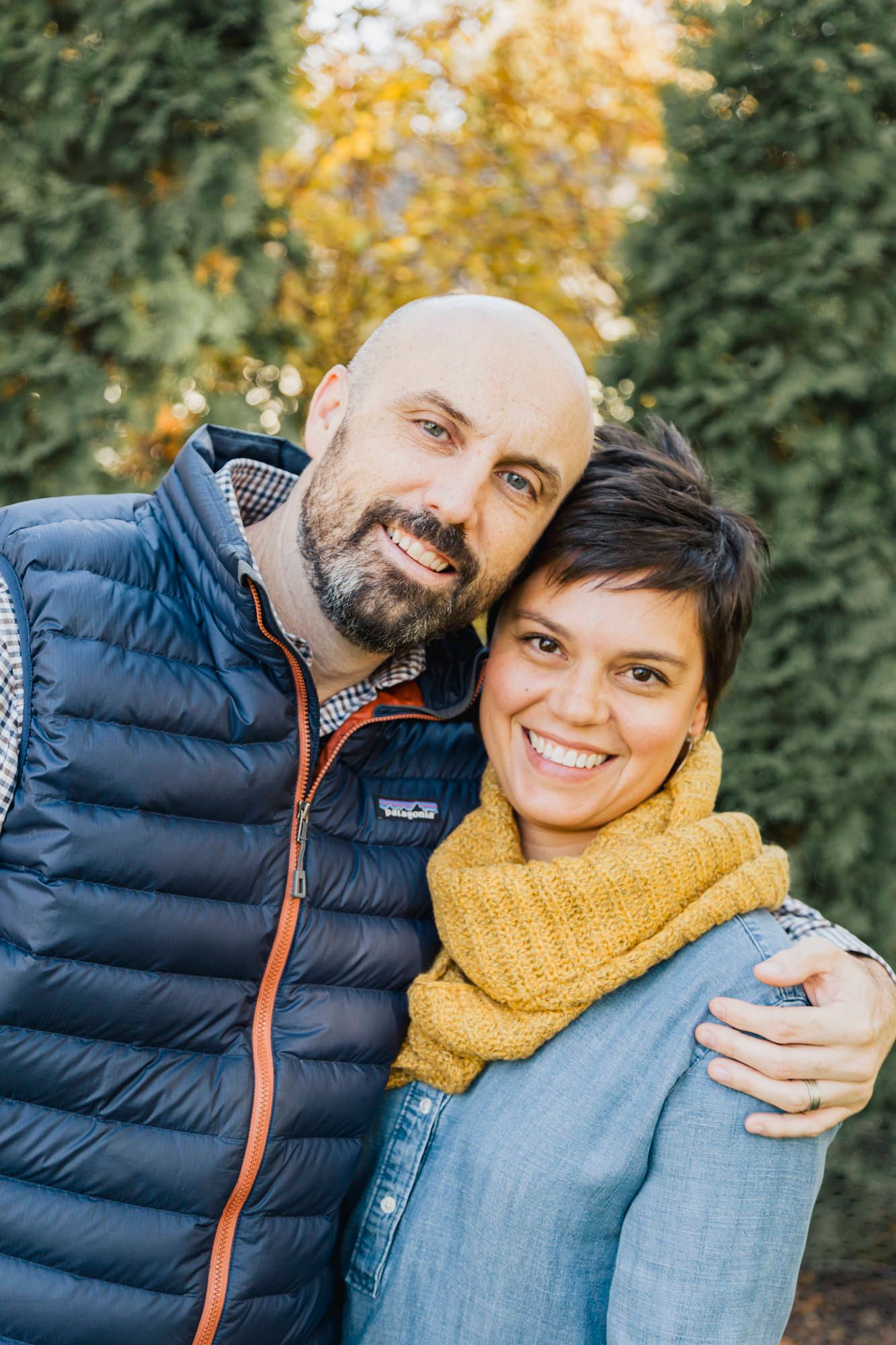 Couple in casual winter wear embrace and smile at camera outdoors.