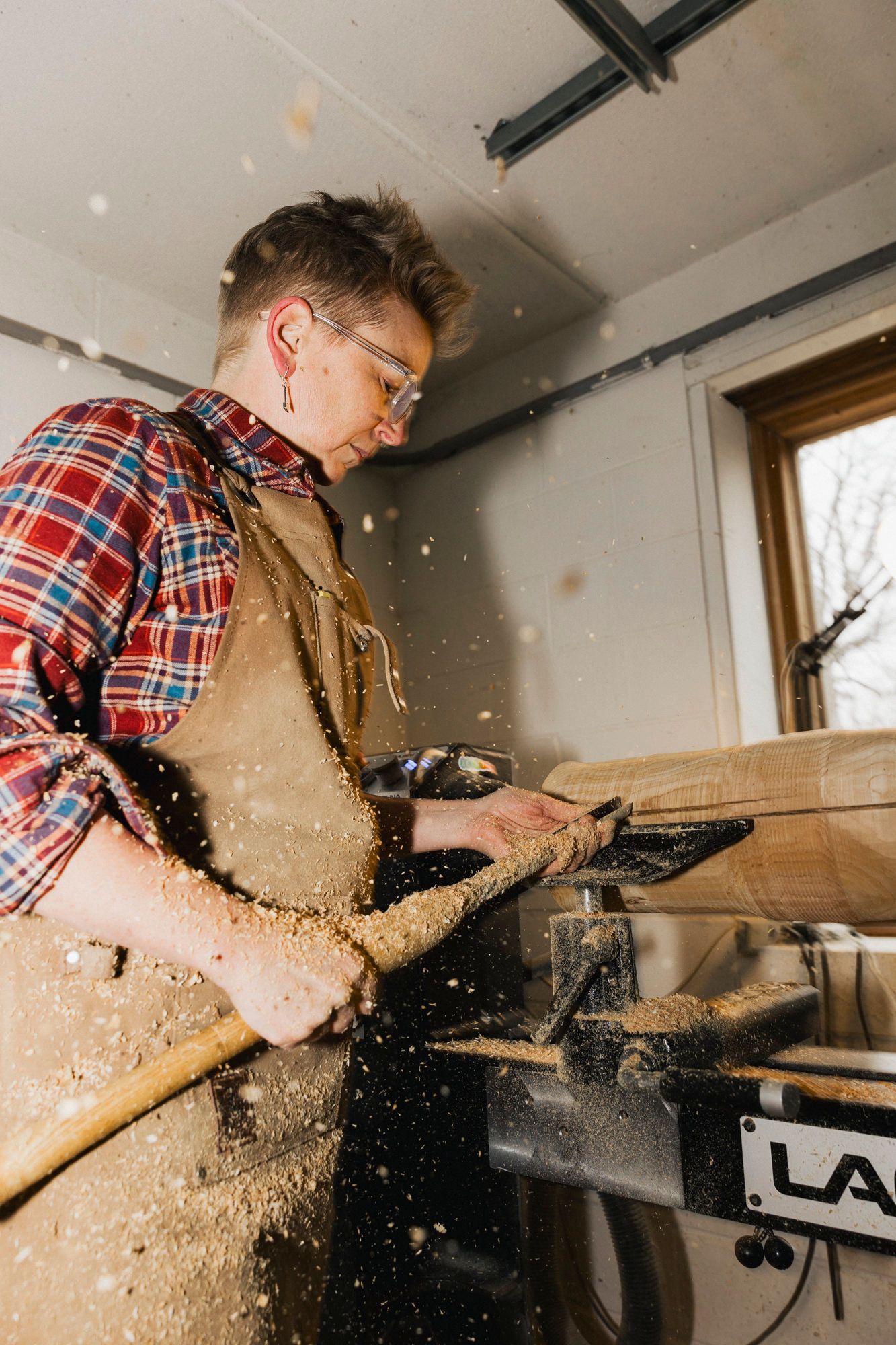 Woodworker in protective gear using power tools with sawdust flying in workshop.