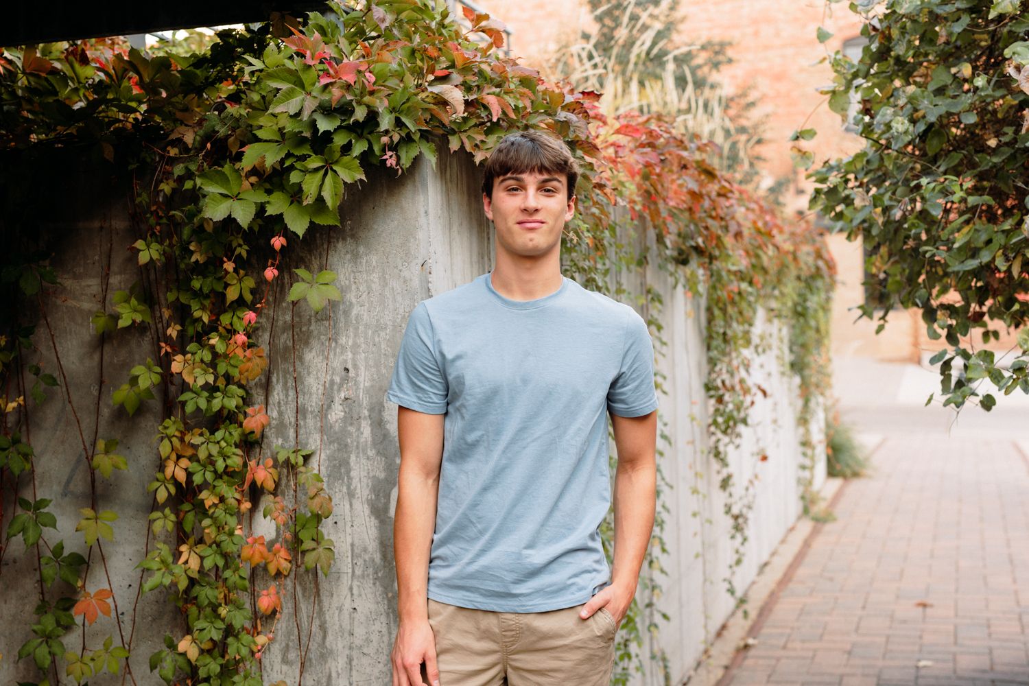 Casual outdoor portrait against brick wall with climbing vines and terracotta tones.